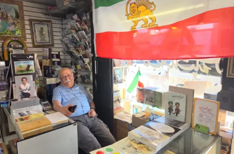 Sam Beykzadeh, seorang warga Amerika keturunan Iran yang mengelola toko buku di Los Angeles, duduk di bawah bendera Iran pra-revolusi Islam di tokonya,
