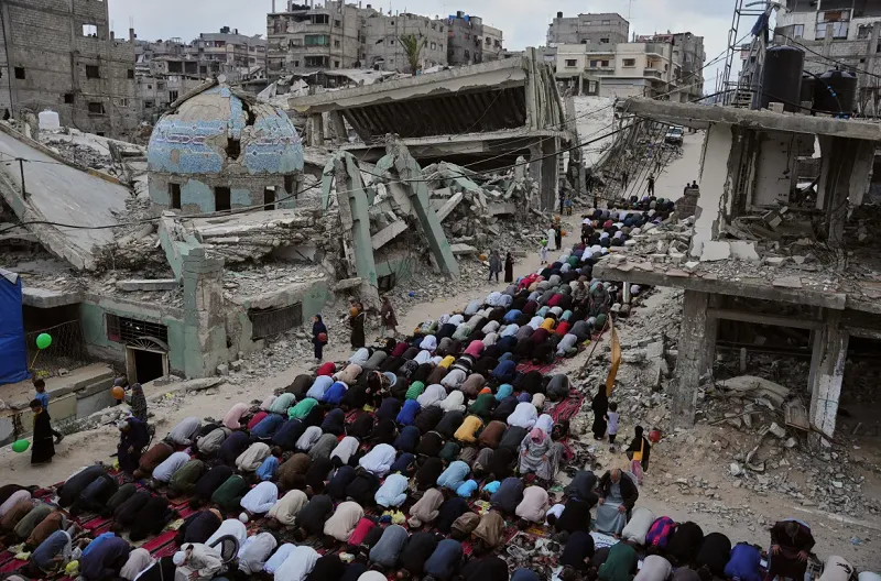 Warga Palestina melaksanakan salat Idul Adha di samping reruntuhan masjid yang hancur akibat bombardir Israel di Khan Younis, Jalur Gaza selatan