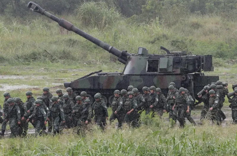 Para tentara bergerak melewati sebuah howitzer swa-gerak selama latihan menembak langsung militer di Kota Taichung, Taiwan